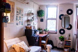 Dorm room with mirror, records, and botanical posters on the wall. White futon against the wall and a coffee table with flowers is in the middle.