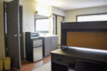 University Towers bedroom with a desk, chair, mini-fridge and microwave combo with a sink and mirror next to it.