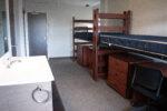 sink and mirror on the left of the room with two beds and all furniture on the rights side of the room.