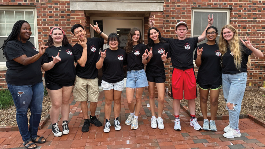 Village mentors for the exploratory students village standing as a group with their hands in the "wolfie" symbol. 